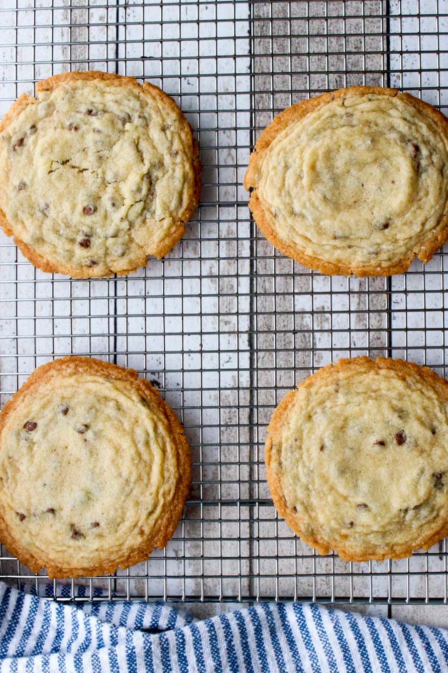 Four giant chocolate chips cookies on a cooling rack with a blue and white towel