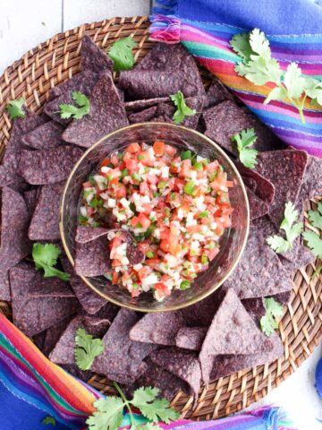 pico de gallo in a bowl surround by blue tortilla chips and fresh cilantro leaves