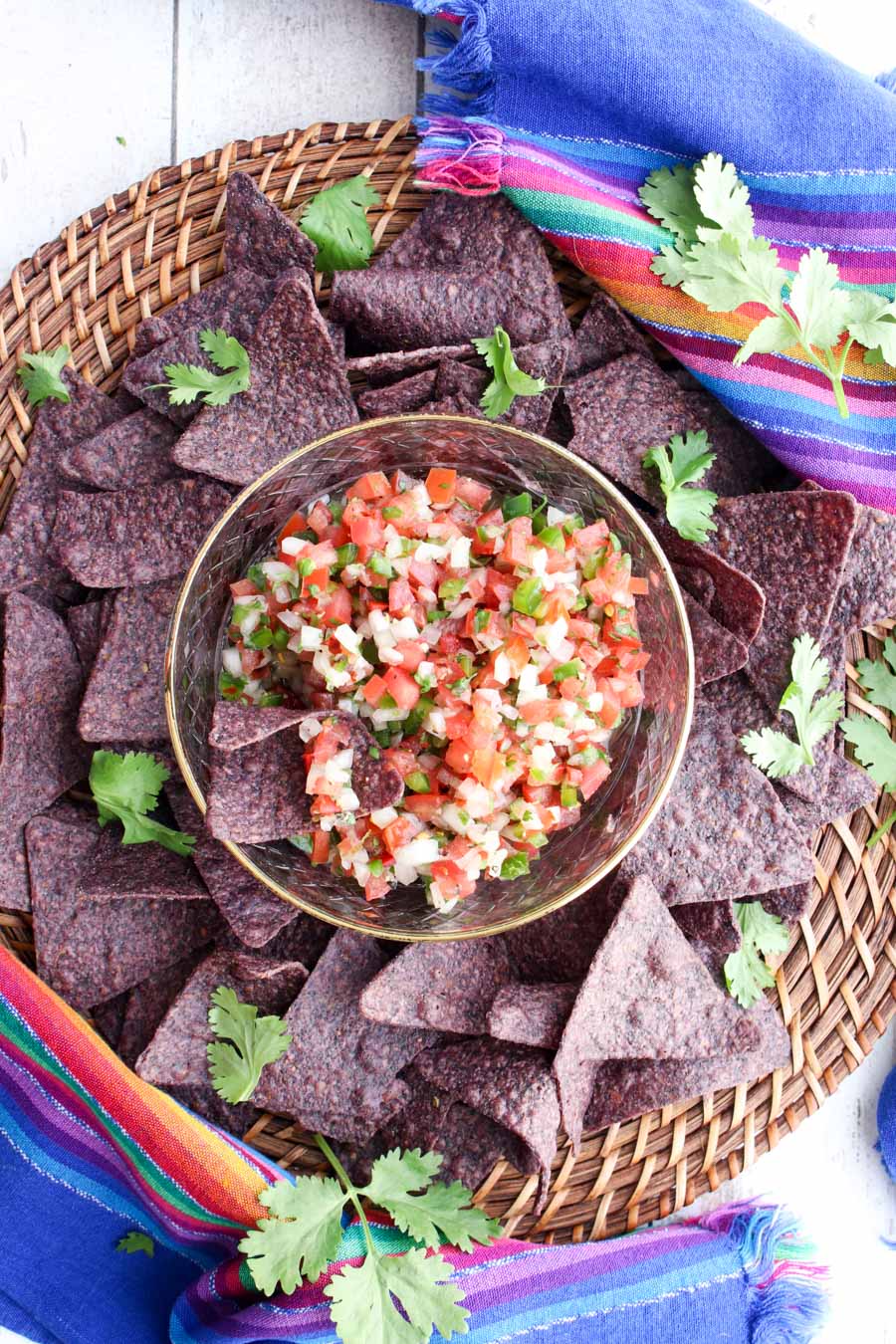 pico de gallo in a bowl surround by blue tortilla chips and fresh cilantro leaves