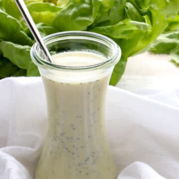 a jar of salad dressing with a head of lettuce in the background