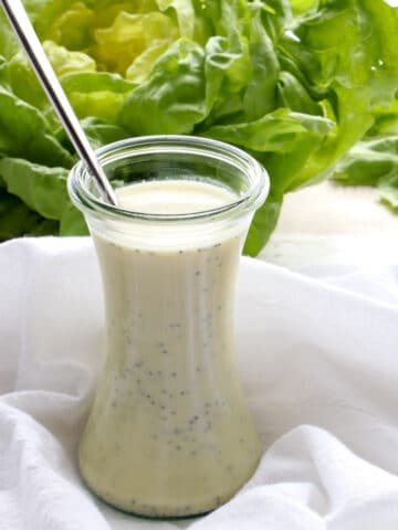 a jar of salad dressing with a head of lettuce in the background