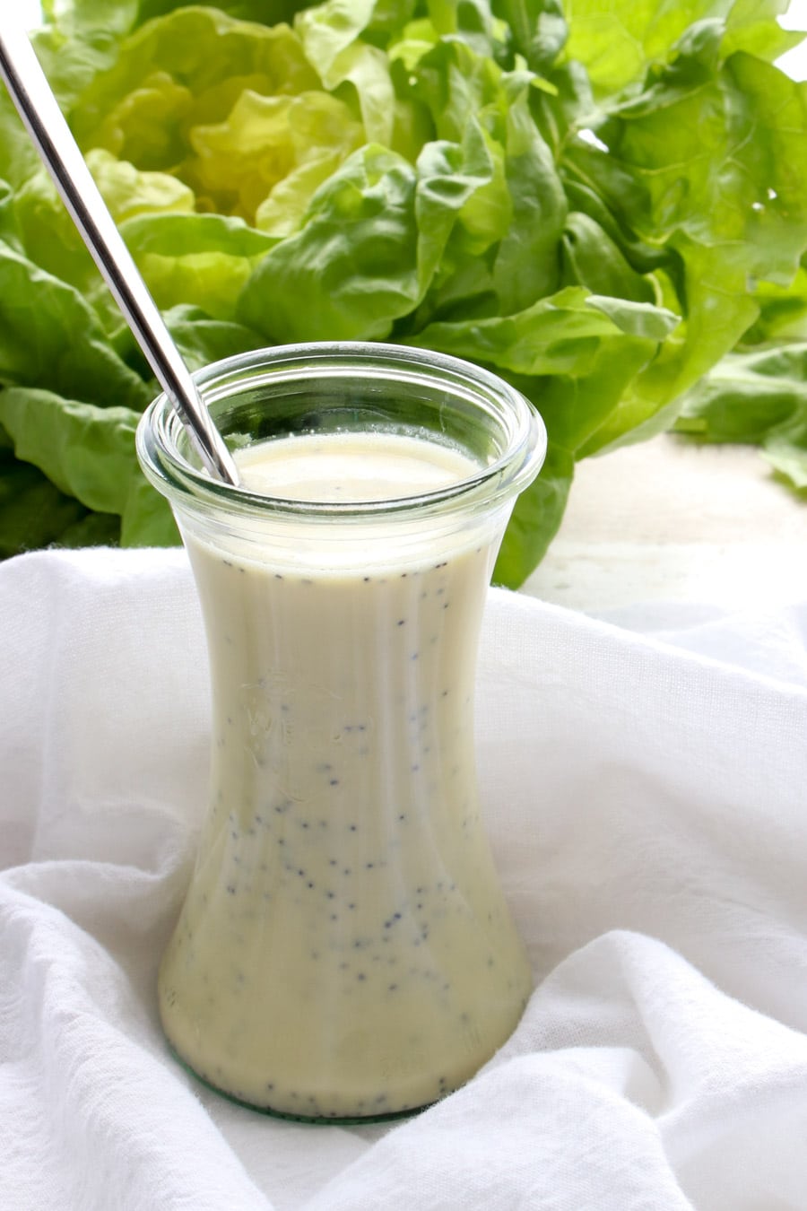 a jar of salad dressing with a head of lettuce in the background