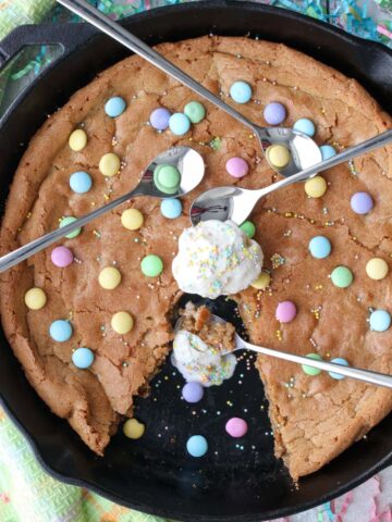 Cookie in a skillet with a scoop of ice cream on top and three spoons