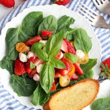 strawberry caprese salad on a white plate with a slice of toasted bread