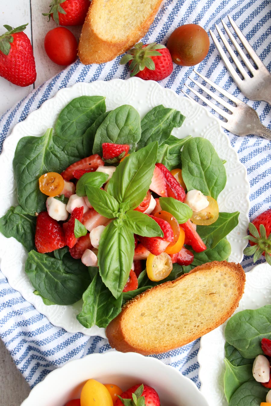 strawberry caprese salad on a white plate with a slice of toasted bread