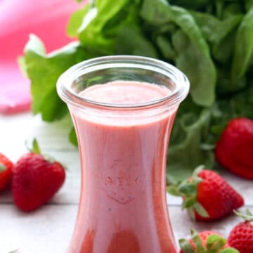 jar of strawberry vinaigrette surrounded by whole strawberries and a head of lettuce in the background