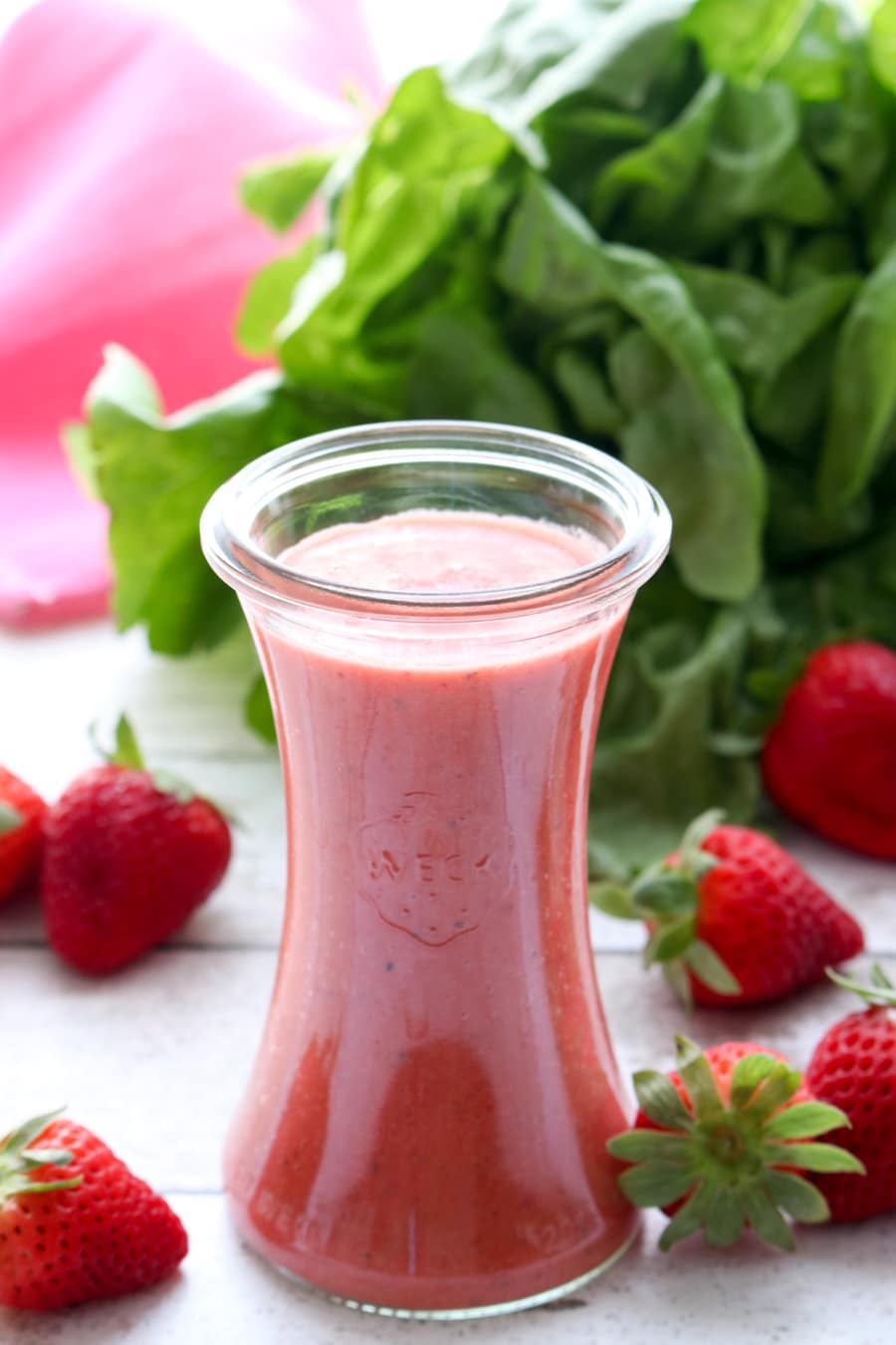 jar of strawberry vinaigrette surrounded by whole strawberries and a head of lettuce in the background