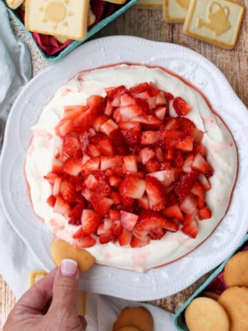 woman's hand dipping a cookie into strawberry cheesecake dip