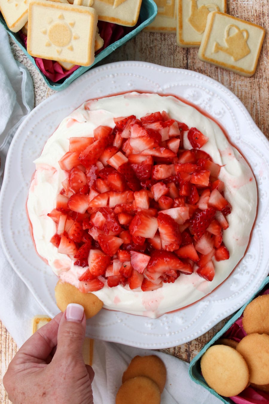 woman's hand dipping a cookie into strawberry cheesecake dip