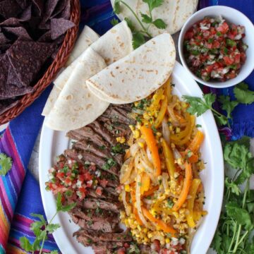 platter of beef fajita with peppers, onions, corn and soft tortillas