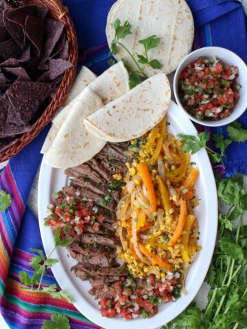 platter of beef fajita with peppers, onions, corn and soft tortillas