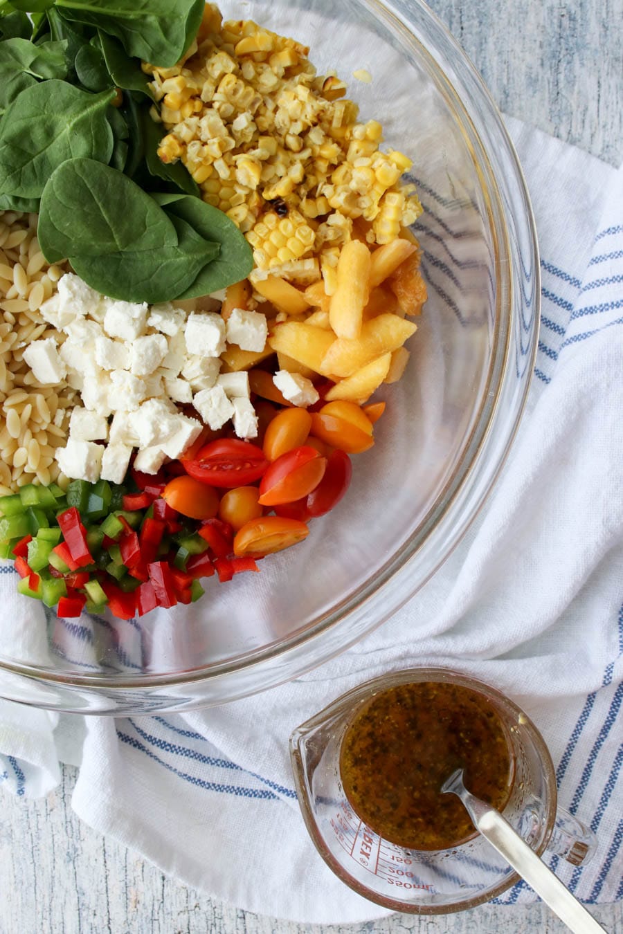 bowl of orzo salad ingredients with dressing on the side