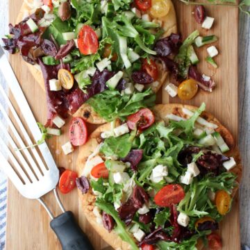 2 Greek Salad Flatbreads on a cutting board with wire spatula