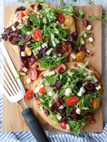 2 Greek Salad Flatbreads on a cutting board with wire spatula