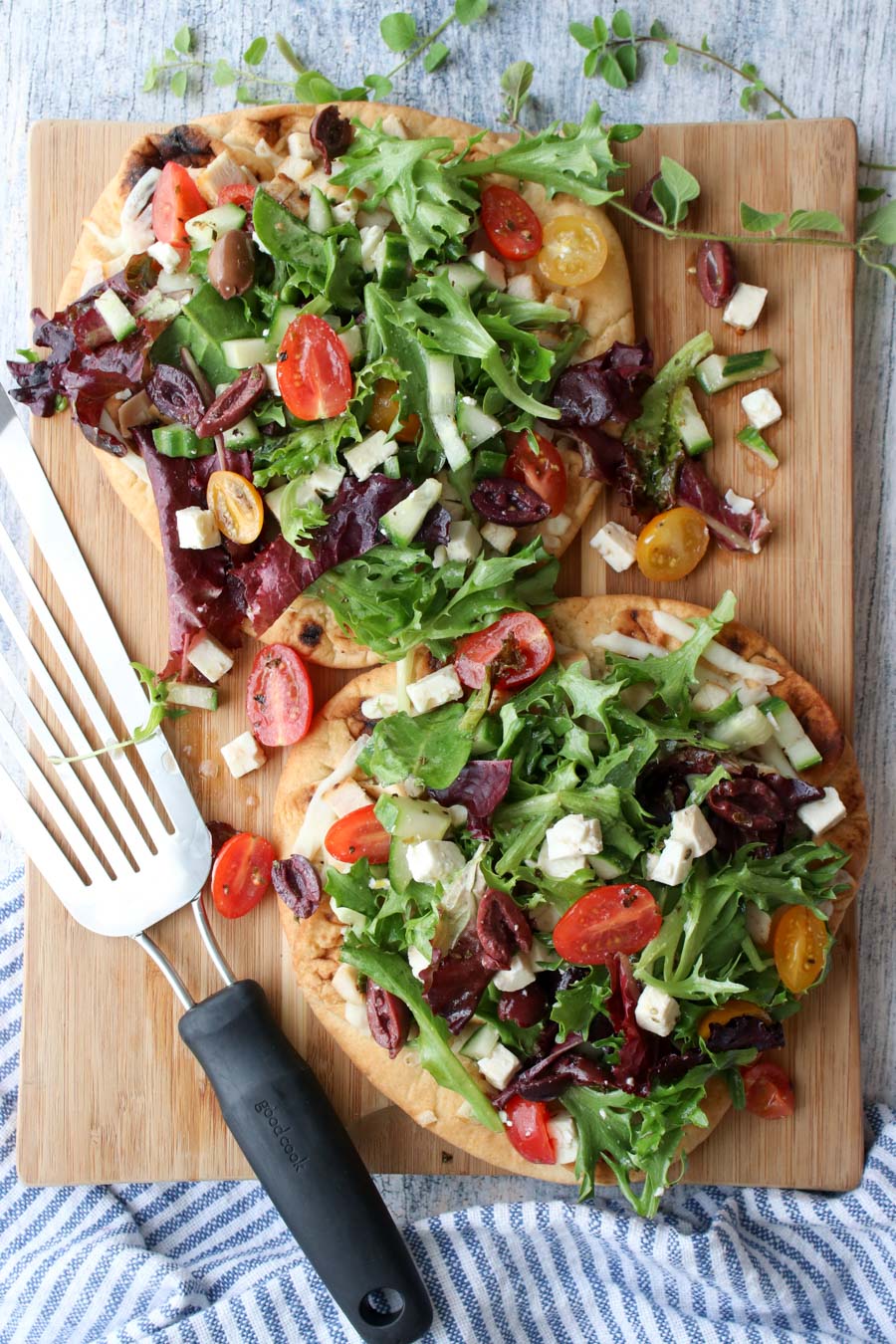 2 Greek Salad Flatbreads on a cutting board with wire spatula