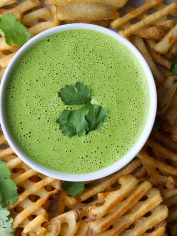 bowl of green cilantro sauce surrounded by waffle fries