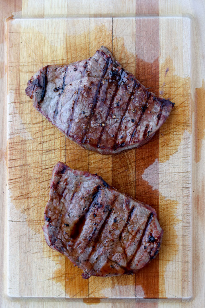 two grilled steaks on a large cutting board