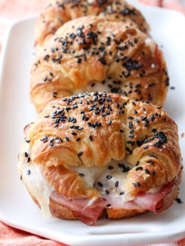 ham and cheese croissant sandwiches lined up on a white plate