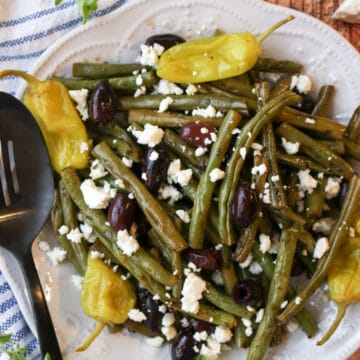 a plate of roasted green beans with olives and peppers