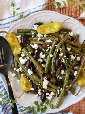 a plate of roasted green beans with olives and peppers