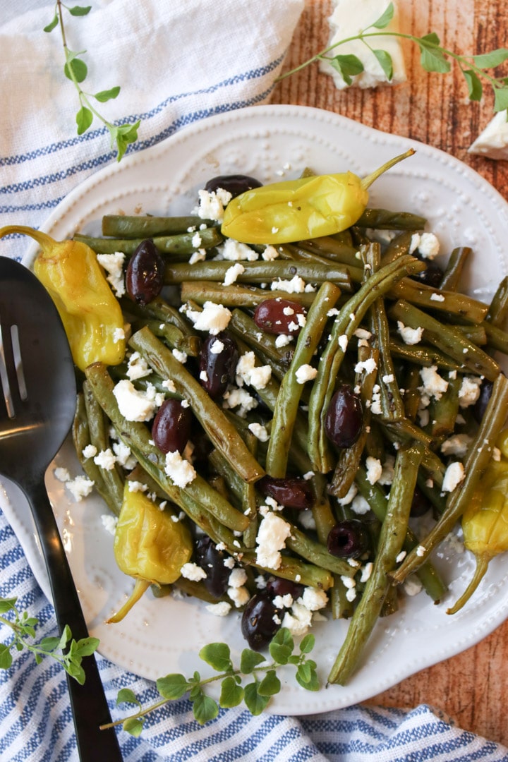 a plate of roasted green beans with olives and peppers