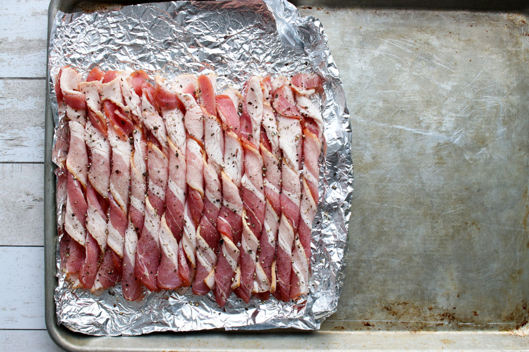 cookie sheet half covered with bacon strips that are curled