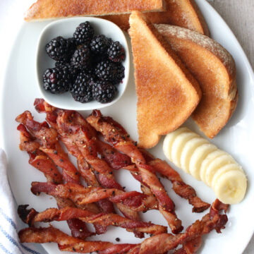 White plate with bacon, banana slices, toast, blackberries