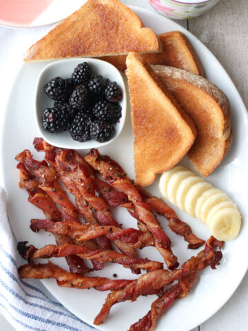 White plate with bacon, banana slices, toast, blackberries