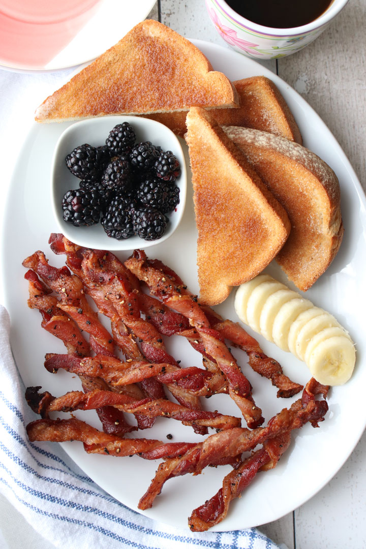 White plate with bacon, banana slices, toast, blackberries