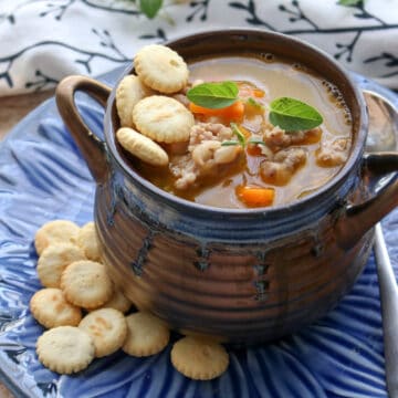 Bowl of white bean and sausage soup in a brown soup dish on a blue plate