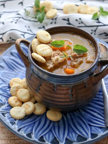 Bowl of white bean and sausage soup in a brown soup dish on a blue plate