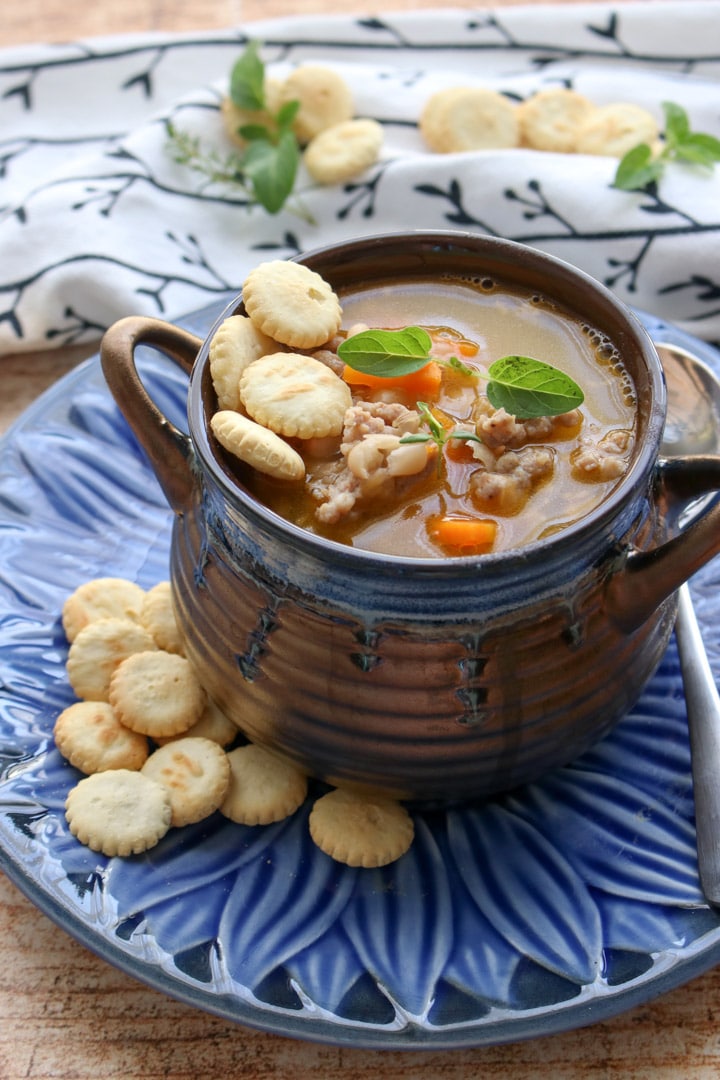 Bowl of white bean and sausage soup in a brown soup dish on a blue plate