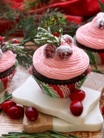 Pink Cranberry buttercream on a chocolate cupcake decorated with sugared cranberries and sugared rosemary