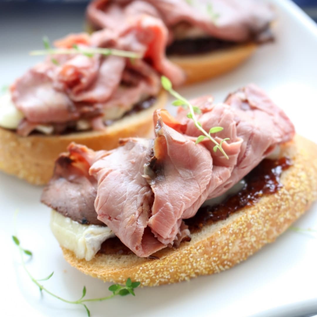 2 pieces of toast topped with fig jam, brie cheese, and london broil beef