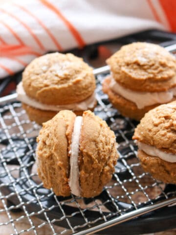 four gingerbread sandwich cookies on a baking rack. One cookie turned on it's side