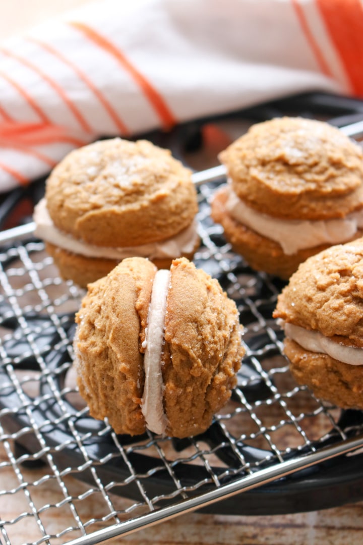 four gingerbread sandwich cookies on a baking rack. One cookie turned on it's side