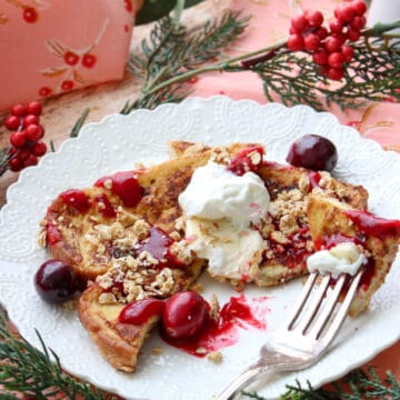 Lacy white plate with a slice of eggnog french toast and cranberry syrup