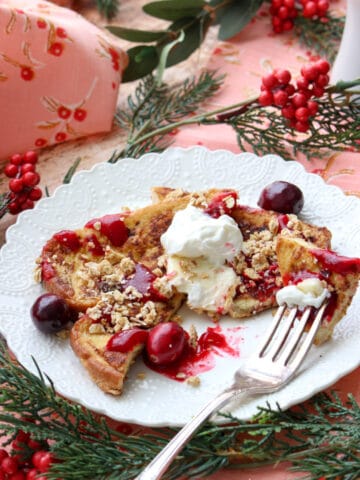 Lacy white plate with a slice of eggnog french toast and cranberry syrup