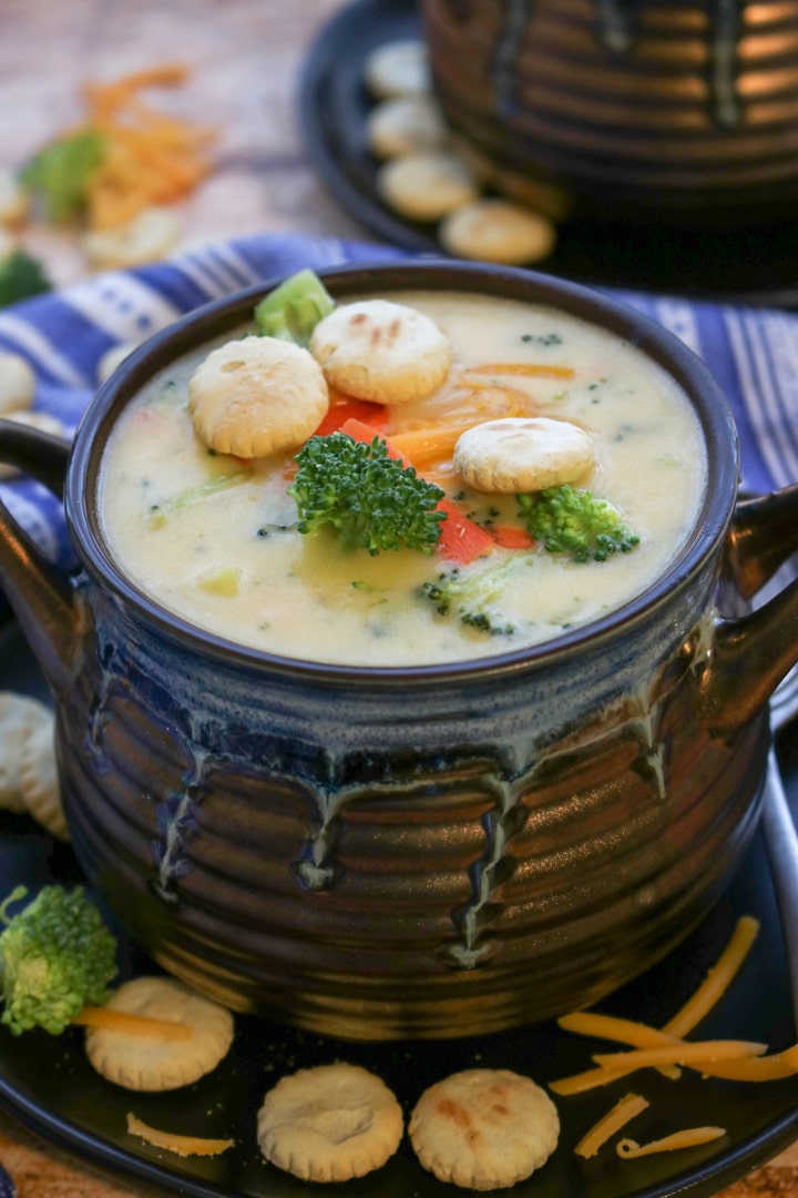 blue and brown soup bowl with broccoli cheese soup topped with crackers, broccoli, carrots