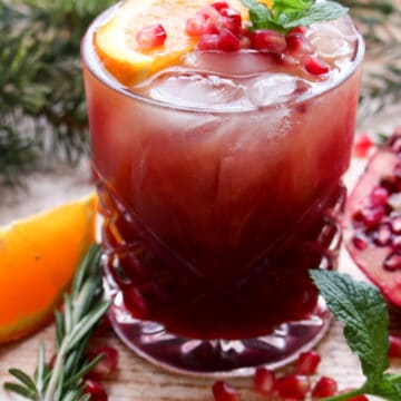 Pomegranate vodka cocktail topped with fresh orange slice, pomegranate arils, fresh mint and rosemary