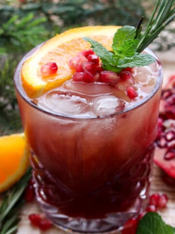 Pomegranate vodka cocktail topped with fresh orange slice, pomegranate arils, fresh mint and rosemary