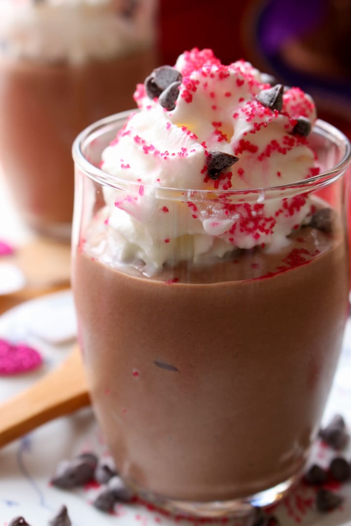 close up shot of a jar of chocolate tofu mousse topped with whipped cream and sprinkles