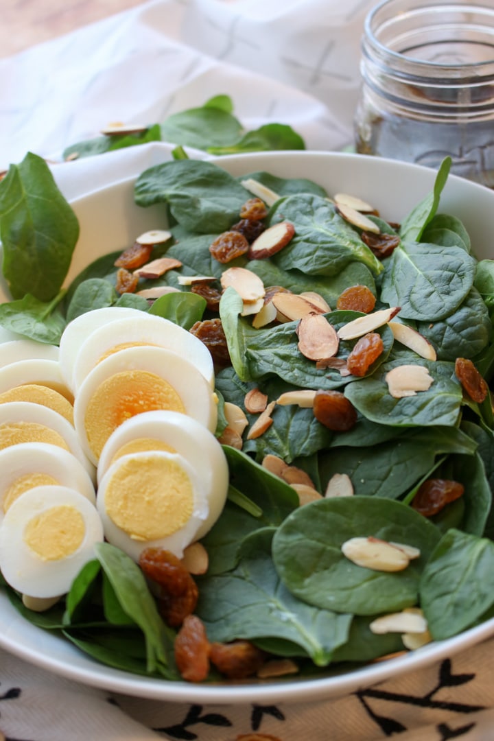 close up shot of spinach salad with hardboiled eggs, raisins, and almonds