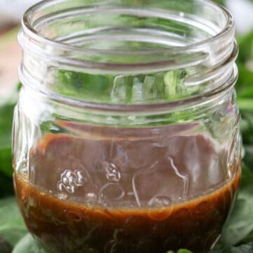 jar of dark mango salad dressing sitting on spinach greens