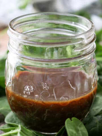 jar of dark mango salad dressing sitting on spinach greens