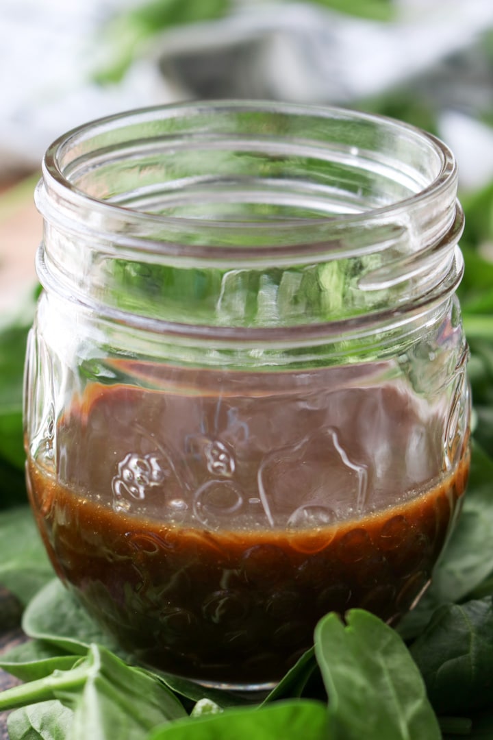 jar of dark mango salad dressing sitting on spinach greens