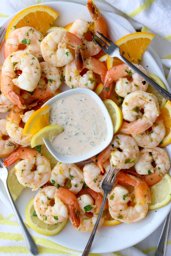 shrimp and lemons on a white platter with a pink sauce