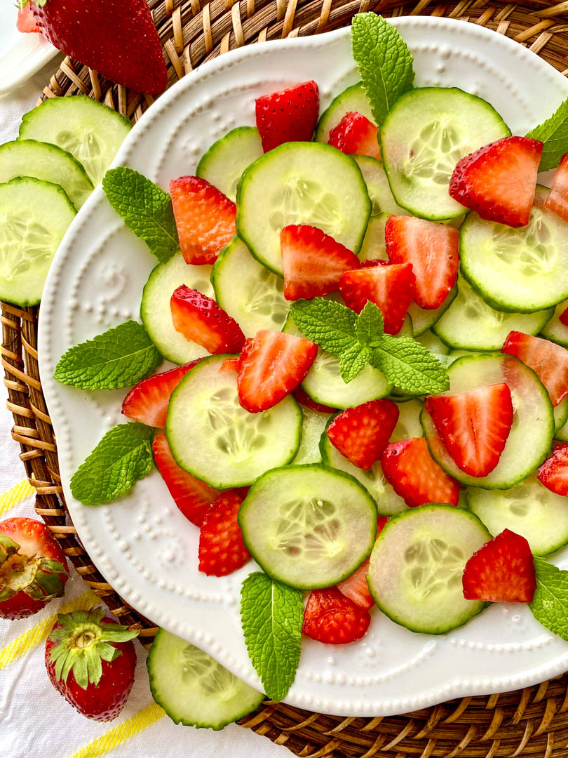 Sliced strawberries and cucumber on a white plate garnished with mint leaves