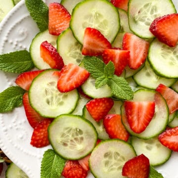 Sliced strawberries and cucumber on a white plate garnished with mint leaves