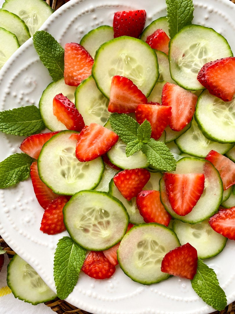 Sliced strawberries and cucumber on a white plate garnished with mint leaves